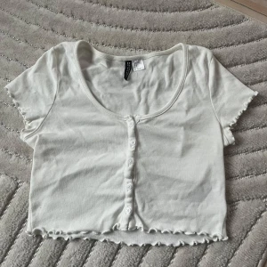 Vit croppad topp med knappar - Supersöt vit croppad topp med korta ärmar och knappar framtill. 