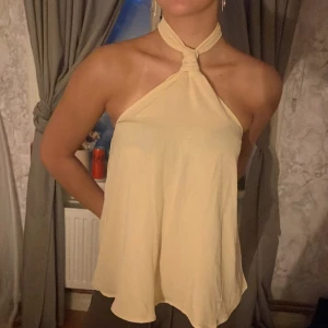 Ljusgul halterneck linnetopp - Säljer en ljusgul halterneck topp med knyt i nacken och lös passform. Toppen är ärmlös och har en flowy, luftig känsla som passar perfekt till varma dagar. Materialet känns lätt och svalt mot huden. Perfekt för dig som gillar stilrena och enkla plagg med en twist.💗Köote här på Plick men blev inte nöjd💕