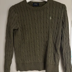 Olivgrön stickad tröja Polo Ralph Lauren - Säljer en olivgrön kabelstickad tröja från Polo Ralph Lauren. Tröjan har rund halsringning, långa ärmar. Nytt skick har endast använt några gånger!
