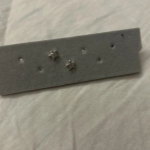 Silvriga stjärnörhängen i miniformat - Säljer ett par små örhängen i form av stjärnor i silverfärg. Perfekta för dig som gillar minimalistiska smycken med en touch av stjärnglans. Snygga att bära till vardags för en subtil men cool detalj.