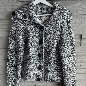 Grovstickad kofta från Nümph - Säljer en grovstickad kofta från Nümph i svartvitt melerat garn. Koftan har stora bruna knappar framtill och en bred krage. Storlek S. 