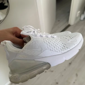 Nike Air 270 helvita sneakers - Nike Air 270 sneakers i helvitt med ventilerande mesh-ovandel, tydlig Air Max-sula och snygga detaljer. Skorna har snörning och en modern, sportig look med rund tå och platt sula. Perfekta för dig som gillar stilrena och bekväma sneakers.