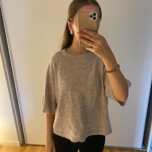 Beige stickad tröja med vida ärmar - Mysig beige stickad tröja med rund halsringning och trekvartsärmar. Tröjan har en loose passform och är perfekt för lager-på-lager under höst och vår. Enkel och stilren design som passar till det mesta.