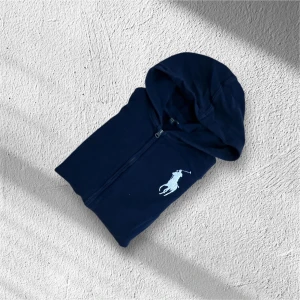 Mörkblå hoodie från Polo Ralph Lauren  - Snygg mörkblå hoodie från Polo Ralph Lauren med vit polospelare på bröstet, amerikansk flagga på ärmen och stor röd siffra 3 på ryggen. Utmärkt skick, inga fläckar eller hål. Storlek 18-20 barnstorlek, motsvarar S/M i vuxenstorlek. Pris: 849 (förhandlingsbart!!)
