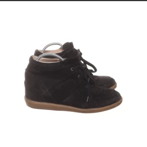 Svarta kilklackade sneakers i mocka - Säljer ett par svarta sneakers med kilklack och snörning. Skorna har en ovandel i mocka och en brun gummisula. Lite slitna