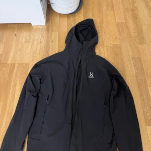 Svart vindjacka från Haglöfs, M - Säljer en svart vindjacka från Haglöfs i storlek M. Jackan har huva, hel dragkedja framtill och två sidofickor med dragkedja. Tillverkad i ett lätt och smidigt syntetmaterial som passar perfekt för utomhusaktiviteter. Enkel och stilren design med Haglöfs-logga på bröstet.perfekt nu till hösten (: