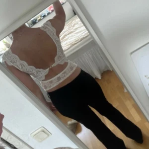 Vit spetsblus med öppen rygg - Supersöt vit blus i spets med djup v-ringning och breda axelband. Toppen har en öppen rygg med fina spetsdetaljer och knäppning bak. Perfekt för dig som vill sticka ut med en romantisk och feminin look.