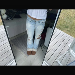 Ljusblå slitna bootcut jeans Coquette - Säljer ett par ljusblå bootcut jeans från Coquette med flera slitningar och hål på benen. Jeansen har låg midja och klassisk femficksmodell. Perfekta för dig som gillar en avslappnad och trendig look.