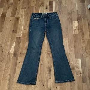 Rock & Roll Denim bootcut jeans blå - Blå bootcut jeans från Rock & Roll Denim med snygga kontrastsömmar, midwaist/lowwaist passform och broderade detaljer på fickorna. Bakfickorna har coolt broderi med tjurmotiv och framfickan har ett mönstrat tyg. Perfekta för dig som gillar western vibe.
