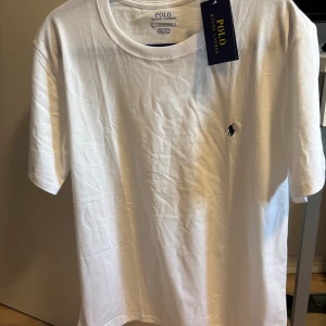 Vit t-shirt från Polo Ralph Lauren - Klassisk vit t-shirt från Polo Ralph Lauren med broderad marinblå logga på bröstet. T-shirten har rund halsringning och korta ärmar. Tillverkad i mjuk bomull för en skön och avslappnad stil. Storlek XL men passar även L 