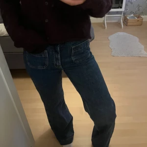 Mörkblå wide jeans med stora fickor - Säljer ett par mörkblå jeans med breda ben och stora fyrkantiga fickor både fram och bak. Jeansen har hög midja och är tillverkade i klassiskt denimtyg. Perfekta för dig som gillar en avslappnad och trendig look.
