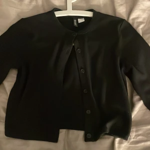 Svart kofta från Divided  - Enkel svart kofta från Divided H&M med rund halsringning och knappar framtill. Klassisk och stilren modell med lång ärm, perfekt att slänga över en topp eller klänning. Mjuk och bekväm, passar till många olika outfits!💞