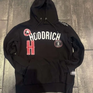 Svart hoodie från Hoodrich - Svart hoodie från Hoodrich i storlek M med stora vita och röda tryck och broderade detaljer framtill.
