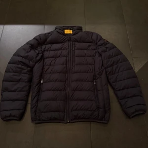 Svart pufferjacka från Parajumpers - Säljer en svart pufferjacka från Parajumpers i superlätt material. Jackan har horisontella sömmar, dragkedja framtill och två sidofickor med dragkedja. Perfekt för dig som vill ha en stilren och varm jacka med sportig känsla.