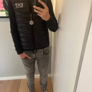 Svart dunväst från EA7 Emporio Armani - Snygg svart dunväst från EA7 Emporio Armani med quiltad design och hög krage. Västen har dragkedja framtill, logga på bröstet och medföljande förvaringspåse. Perfekt för lager-på-lager och streetstyle.