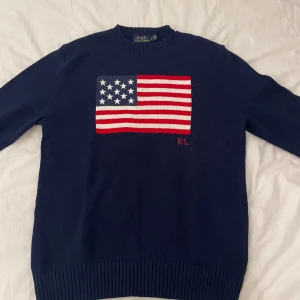 Mörkblå stickad tröja Polo Ralph Lauren - Mörkblå stickad tröja från Polo Ralph Lauren med amerikansk flagga. Tröjan sitter mer som m skulle jag säga. Skriv vid funderingar, pris är ej hugget i sten!😁