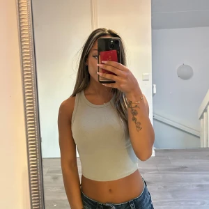 Beige ribbad croppad linnetopp - Snygg beige croppad linnetopp med ribbad struktur och rund halsringning. Toppen är ärmlös och har en tight passform som framhäver figuren. Perfekt att matcha med jeans eller kjol för en trendig look.