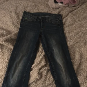 Mörkblå bootcut jeans med grönt märke - Snygga mörkblå jeans från Cheap Monday med bootcut passform och låg midja. Jeansen har slitningar framtill och ett grönt Cheap Monday-märke på bakfickan. Klassisk femficksmodell i stretchig denim som sitter tajt upptill och släpper ut vid benslutet.