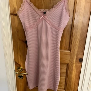 Rosa ribbad kortklänning med spets - Supersöt ljusrosa kortklänning från New Yorker med ribbad struktur, smala axelband och spetsdetaljer längs urringningen.