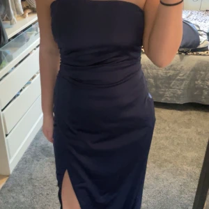 Marinblå axelbandslös långklänning - Säljer en marinblå axelbandslös långklänning från Nelly. Klänningen har en figurnära passform, slits framtill och är tillverkad i ett glansigt, mjukt material som ger en elegant look. Perfekt för dig som vill sticka ut med en stilren och modern vibe.💕