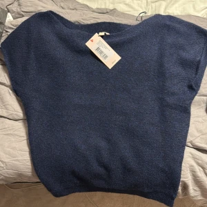 Mörkblå stickad topp med offshoulder - Säljer en mörkblå stickad topp med avslappnad passform och offshoulder-design. Toppen är ärmlös och har en mjuk, lite luddig yta. Perfekt att styla med jeans eller kjol för en chill look. Var lite för stor för mig tyvärr, oanvända 