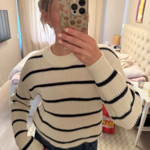 Randig stickad tröja från Gina Tricot - Superfin stickad tröja från Gina Tricot i vitt med svarta horisontella ränder. Tröjan har en bred ribbad mudd i halsen och långa ärmar. Perfekt till vardags och hösten.