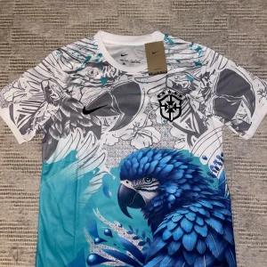 Nike Brasil CBF fotbollströja med papegojmotiv - Unik kortärmad fotbollströja från Nike med Brasil CBF-logga. Tröjan har ett färgstarkt papegojmotiv i blått och grått, med detaljerade blommor och grafiska mönster. Materialet är lätt och andas, Dri-Fit-teknologi för extra komfort. Perfekt för dig som gillar snygga och originella matchtröjor.fler bilder privat.