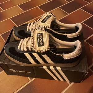 Adidas Wales Bonner Samba sneakers - Unika Adidas Wales Bonner Samba sneakers i svart och beige med klassiska tre ränder på sidan. Skorna har breda snören, detaljerad kontrastsöm och stor plös med Wales Bonner-logga. Ovandel i mocka och skinn, gummisula och retrovibe. Perfekt för dig som vill sticka ut. Ni vet varför de är så billiga 