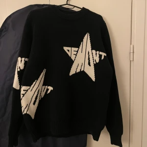 Demont tröja  - Svart stickad tröja från Demont med vit grafisk stjärndesign och text på både fram- och baksida samt ärmar. Rund hals och ribbade muddar vid ärmslut och nederkant. Perfekt för dig som gillar streetwear och vill sticka ut med coolt mönster.