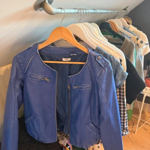 Blå skinnjacka från Resolut - Snygg blå skinnjacka från Resolut med rund hals, dragkedja framtill och två zip-detaljer på bröstet. Jackan har lång ärm, markerade axlar med knapp och elastisk nederkant för en cool siluett. Perfekt för dig som vill sticka ut med färg. Det står storlek L men skulle säga att det är S/M