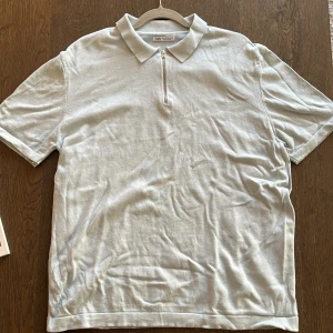 Blå kortärmad pike med zip från Zara - Vit pike från Zara med klassisk krage och halv dragkedja framtill. Modellen är kortärmad och har en stilren, enkel design. 