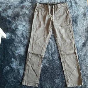 Beige chinos från Bläck, stl 31 - Snygga beige chinos från Bläck i storlek 31. Klassisk rak passform med fickor fram och bak, tillverkade i mjukt bomullsmaterial. Perfekta för en clean och stilren look.