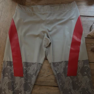 Adidas Stella McCartney leggings L - Snygga leggings från Adidas Stella McCartney i ljusgrått med röda detaljer och blommigt mönster nertill. Tight passform och tillverkade i stretchigt syntetmaterial, perfekta för träning eller när du vill sticka ut.