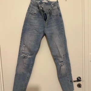 Skinny high rise jeans från Bershka - Ljusblå skinny high rise jeans från Bershka i klassisk femficksmodell. Jeansen har slitna detaljer vid knäna och råa benslut för en trendig look. Tillverkade i denim med dragkedja och knapp framtill.