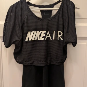 Svart croppad Nike Air topp - Säljer en svart croppad topp från Nike Air med vit logga framtill. Topp i sportig mesh med tunna horisontella ränder, korta ärmar och öppen ryggdetalj. Perfekt för träning eller en sportig look.