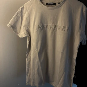 Beige t-shirt från Top Reiter L - Snygg beige t-shirt från Top Reiter i storlek L. Framsidan har ett upphöjt tryck med texten 'TOP REITER' och på ryggen finns en liten isländsk flagga. T-shirten är gjord i mjuk bomull och har klassisk rund hals och korta ärmar.