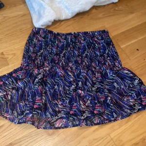 Färgglad kortkjol från Bik Bok - Kortkjol från Bik Bok med färgstarkt abstrakt mönster i blått, lila, rosa, svart och vitt. Kjolen har volang nertill och smockad midja för en bekväm passform. Perfekt för dig som gillar att sticka ut med coola färger och mönster. Har klippt bort storlekslappen men är skit stretchiga och passar mig som har XS/158/164 vanligtvist. Kom privat för mer bilder ❤️❤️