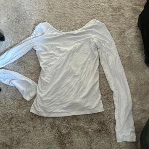 Vit långärmad topp med djup ringning - Säljer en vit långärmad topp med öppen rygg. Toppen har en slim passform och är tillverkad i mjukt bomullsmaterial som känns skönt mot huden. Perfekt att styla med jeans eller kjol för en clean och fräsch look.
