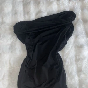 Svart axelbandslös topp - Snygg svart axelbandslös topp med draperad design och figurnära passform. Perfekt för dig som vill sticka ut med en elegant och stilren look. Mjuk och följsam känsla i materialet.