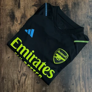 Arsenal Träningströja - Arsenal träningströja i svart med neongula detaljer. Storlek Small. Mycket bra skick – inga fläckar eller skador. Officiell Adidas-modell med “Emirates Fly Better”-tryck. Sval och bekväm passform, perfekt för träning eller som casual streetwear.