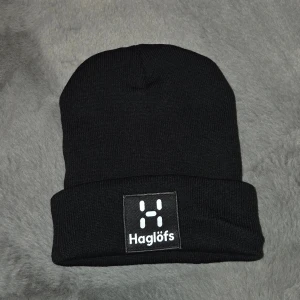 Svart mössa från Haglöfs - Svart ribbstickad mössa från Haglöfs med uppvikt kant och tydlig logotyp framtill. Klassisk och enkel design som passar perfekt till kyliga dagar. Tillverkad i mjukt och stretchigt material för skön passform.