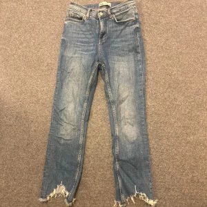 Blå jeans med fransig nederkant från Zara - Snygga blå jeans från Zara med raka ben och fransig, ruffig nederkant. Klassisk femficksmodell med normal passform och knappgylf. Perfekta för en avslappnad och trendig look.