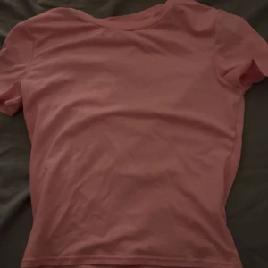 Rosa basic topp - Enkel rosa topp med rund hals och korta ärmar. Modellen är klassisk och passar perfekt till jeans eller shorts. Tillverkad i mjuk bomull för en skön känsla hela dagen.