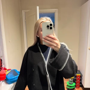 Svart koft/jacka från Gina Tricot - Säljer en svart koft/jacka från Gina Tricot med vita dekorativa sömmar längs kanterna.. Perfekt för lager-på-lager och ger en clean look till din outfit. går att knäppa 