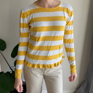 Randig gul och vit tröja från Kids Only - Superfin långärmad tröja från Kids Only med breda gula och vita ränder. Tröjan har rund halsringning och en söt volangkant nertill. Perfekt för dig som gillar färg och vill sticka ut lite extra.