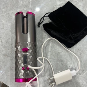 Automatisk trådlös hårlocktång - Snygg och modern automatisk hårlocktång med trådlös funktion, laddningskabel och förvaringspåse. Grå och rosa design med digital display och flera inställningsknappar. 