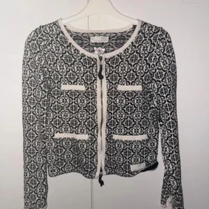 Svartvit stickad kofta Odd Molly - Supersnygg svartvit stickad kofta från Odd Molly med grafiskt mönster, rund hals och dragkedja framtill. Koftan har dekorativa fickor och kontrastfärgade kanter🩷