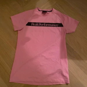 Rosa Peak Performance t-shirt - Säljer en rosa t-shirt från Peak Performance med svart logga över bröstet. Klassisk passform med korta ärmar och rund halsringning. Perfekt för dig som gillar sportiga och stilrena plagg. Materialet är mjuk bomull som känns skönt mot huden.
