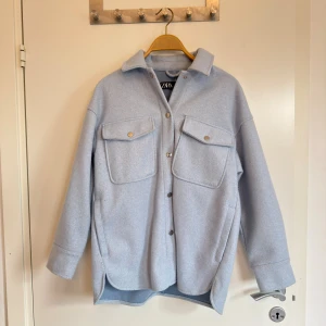 Ljusblå overshirt jacka från Zara i XS - Ljusblå overshirt jacka från Zara i storlek XS. Jackan har två stora bröstfickor med knappar, klassisk krage och knäppning framtill. Tillverkad i mjuk polyester och har en avslappnad, lite oversized passform. Perfekt för lager-på-lager-stil.