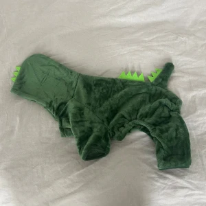 Helt ny hunddräkt - Supermysig grön hoodie till hund, gjord i mjuk fleece med urgulliga drakdetaljer och en liten svans. Perfekt för att göra din hund till en söt liten drake!   Måtten är markerade i tabellen. Den är helt oanvänd - köpte fel storlek och hann inte returnera.